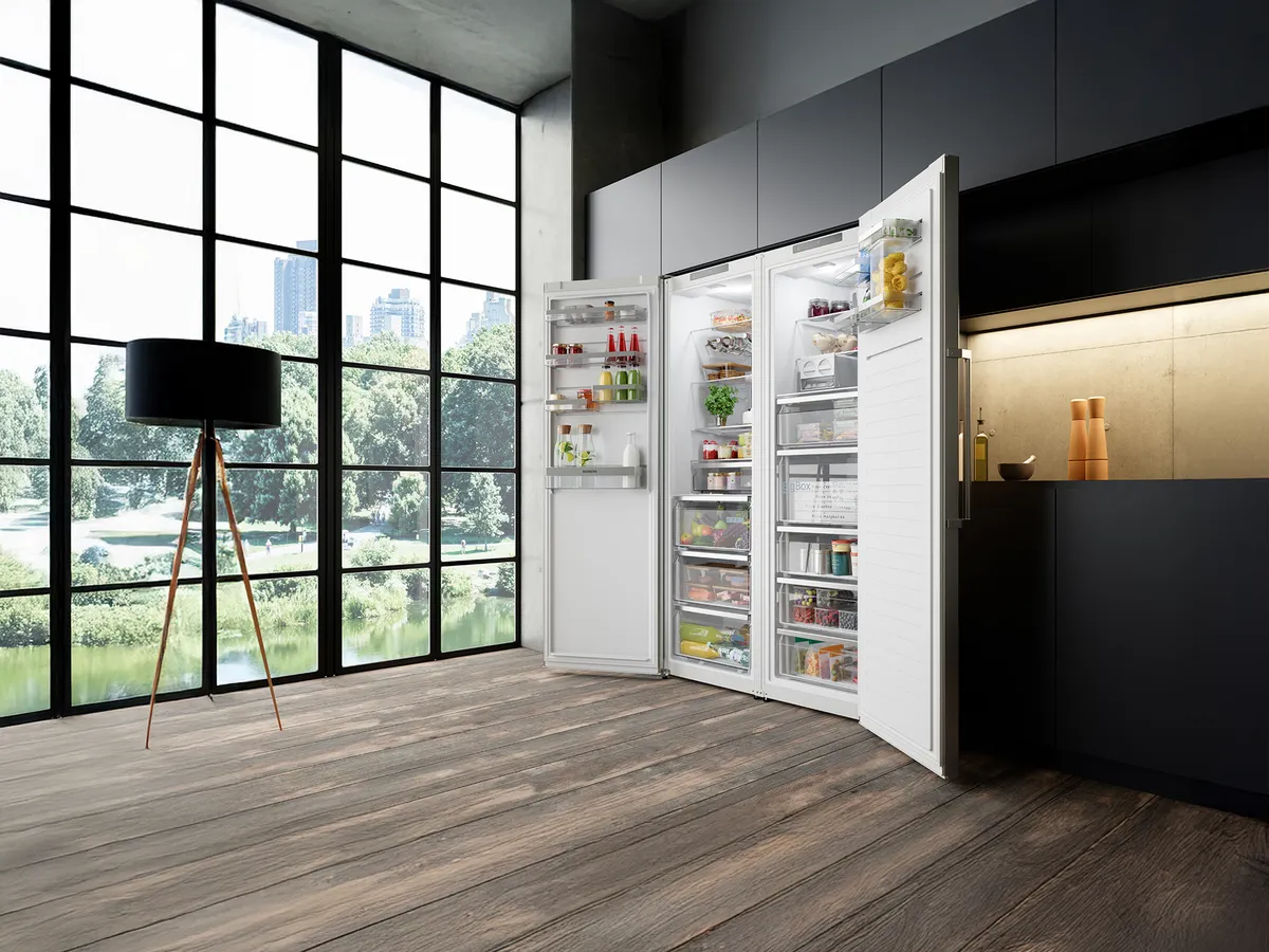 En una amplia cocina abierta con un gran ventanal, un conjunto de frigorífico y congelador de una puerta empotrados en un mueble oscuro, abiertos y con alimentos.