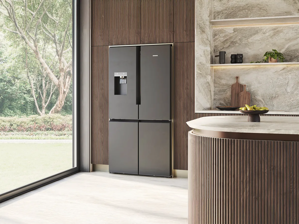 Modern kitchen featuring a sleek black refrigerator, with textured wooden panels and a stone island adorned with a bowl of fruit.