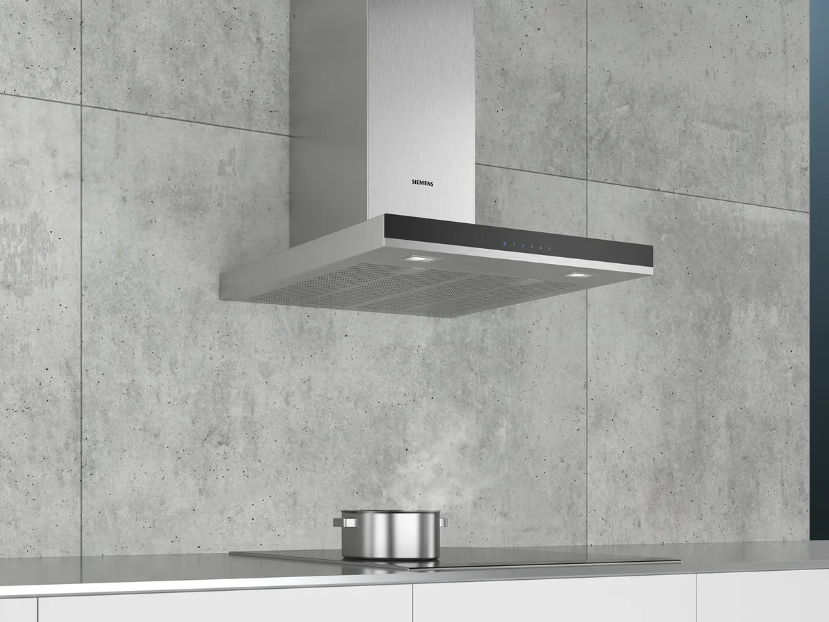 A modern Siemens range hood hangs above a sleek induction cooktop with a pot, set against a concrete wall. 