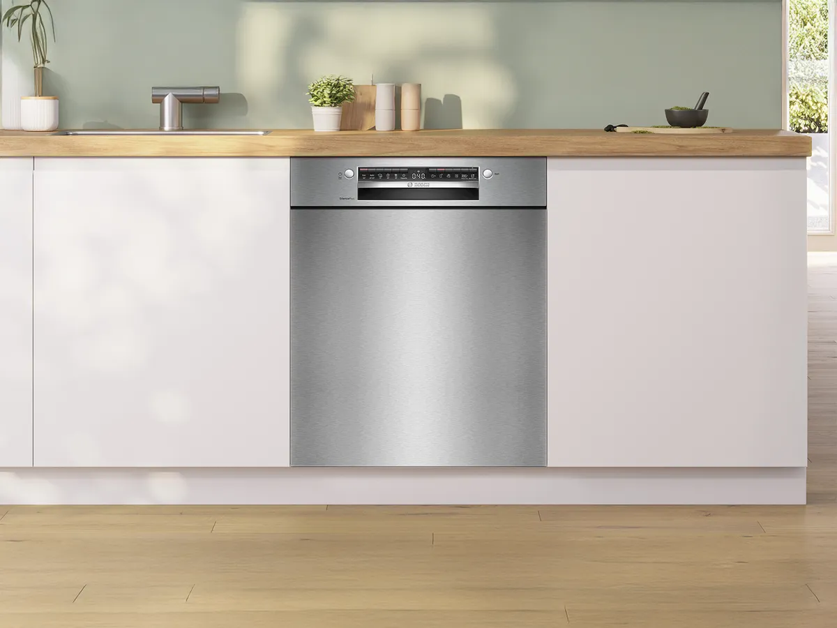 Cucina moderna dotata di un'elegante lavastoviglie in acciaio inox integrata in mobili bianchi, accompagnata da un piano di lavoro in legno e piante.