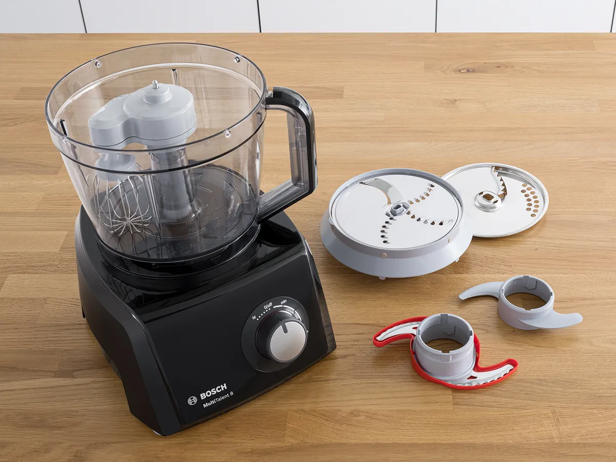 Here's an example:  Black Bosch food processor with its bowl and various blades/discs laid out on a wooden counter.