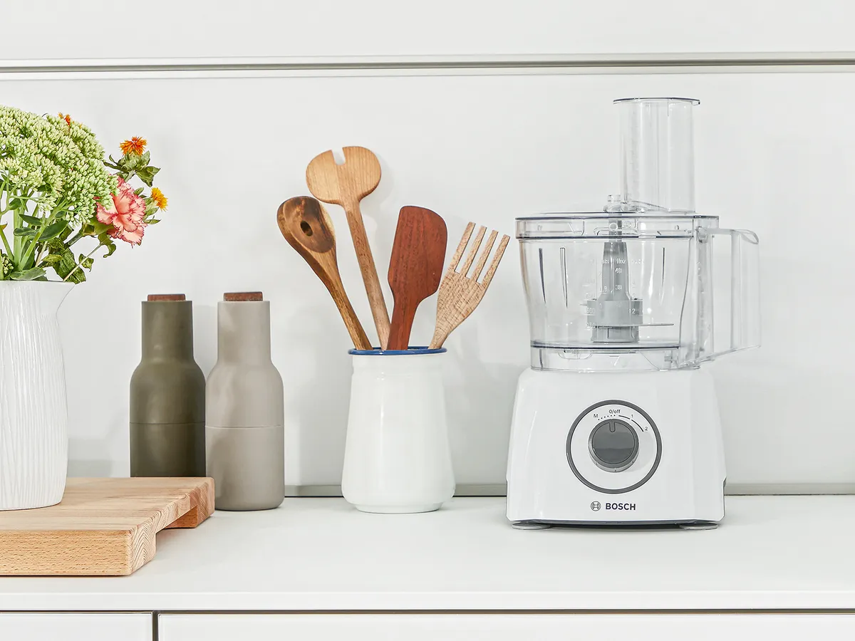 Kompakte Küchenmaschine mit Zubehör auf einer Arbeitsplatte.