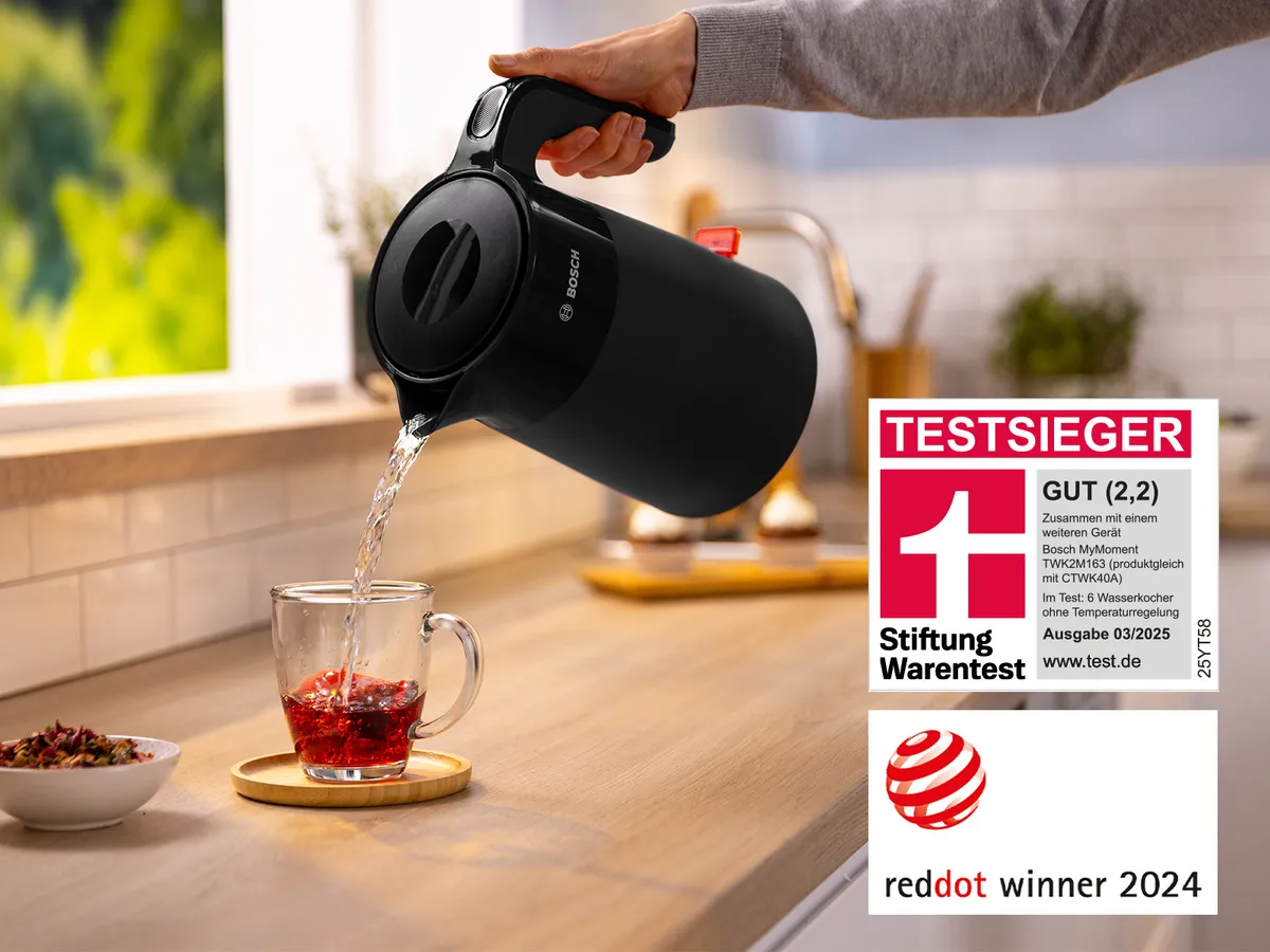 In einem modernen Küchenumfeld gießt eine Person Wasser aus einem eleganten schwarzen Bosch Wasserkocher in ein Teeglas mit Teekräutern.