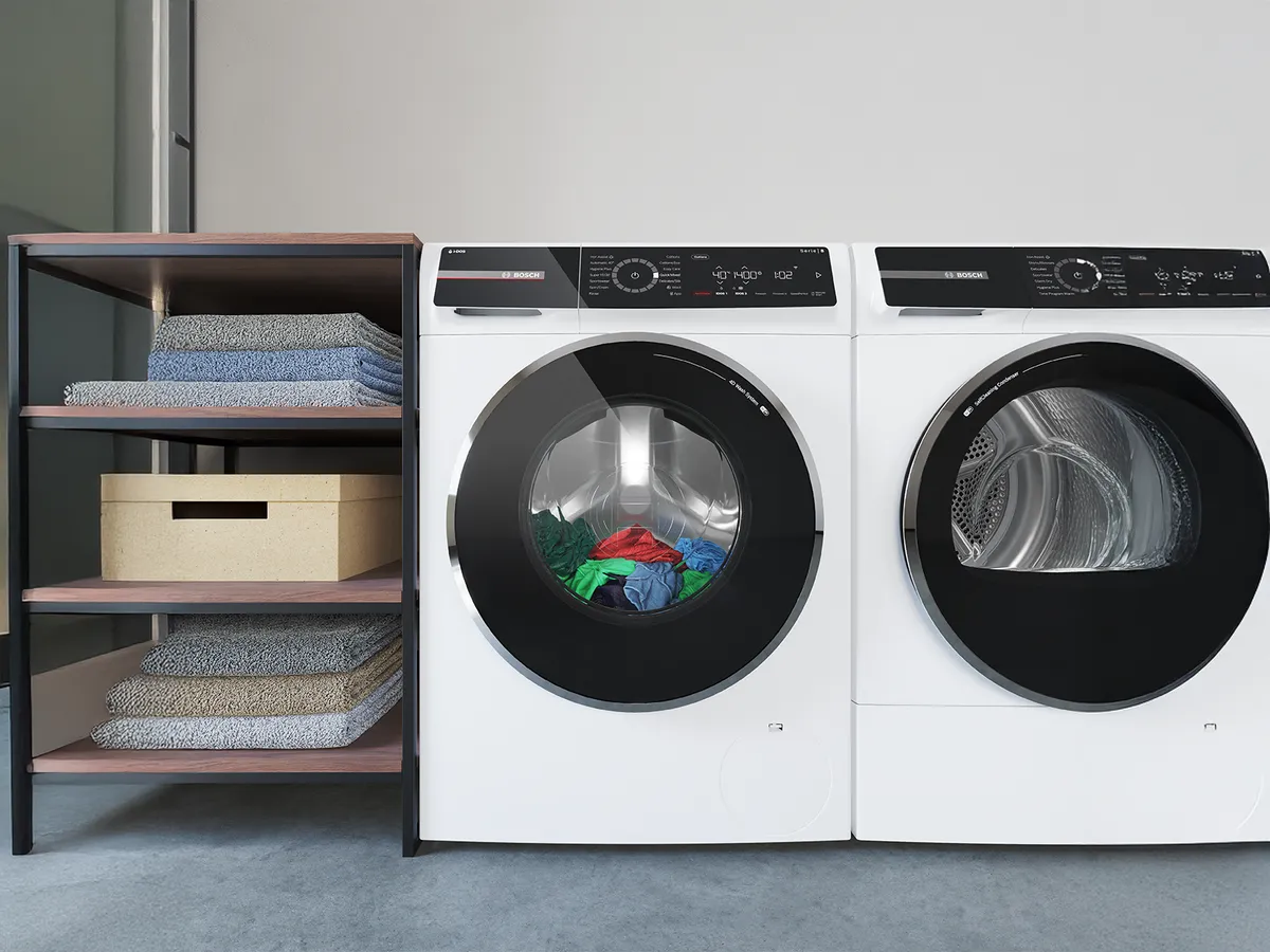 Модерни бяла пералня и сушилня до дървен рафт, подреден със спретнато сгънати кърпи и кутия за съхранение.