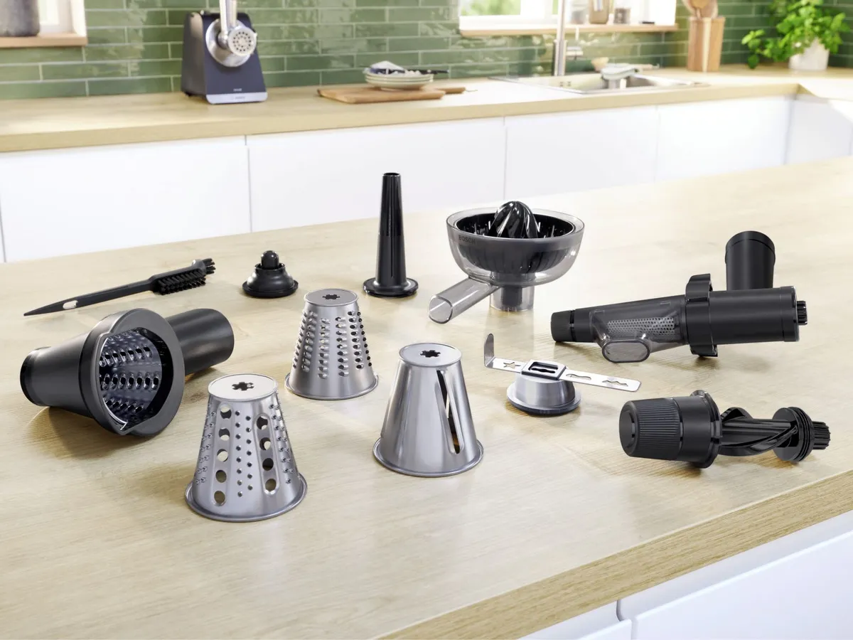 A collection of kitchen tools and attachments on a wooden countertop, including graters, a juicer, and various food preparation gadgets.