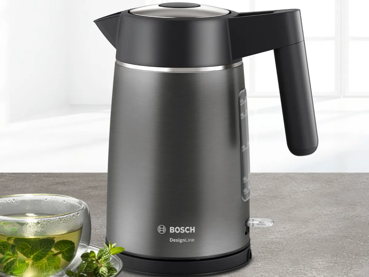 Eleganter Bosch DesignLine Wasserkocher aus Edelstahl auf einem Keramiktisch, daneben steht ein gefülltes dampfendes Teeglas.