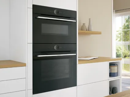A modern gas stovetop with a lit burner producing blue flames, next to an olive oil bottle and wooden spoon.