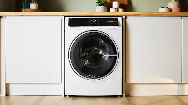 washer dryer combo installed under a wooden countertop, flanked by white cabinetry in a modern laundry room.