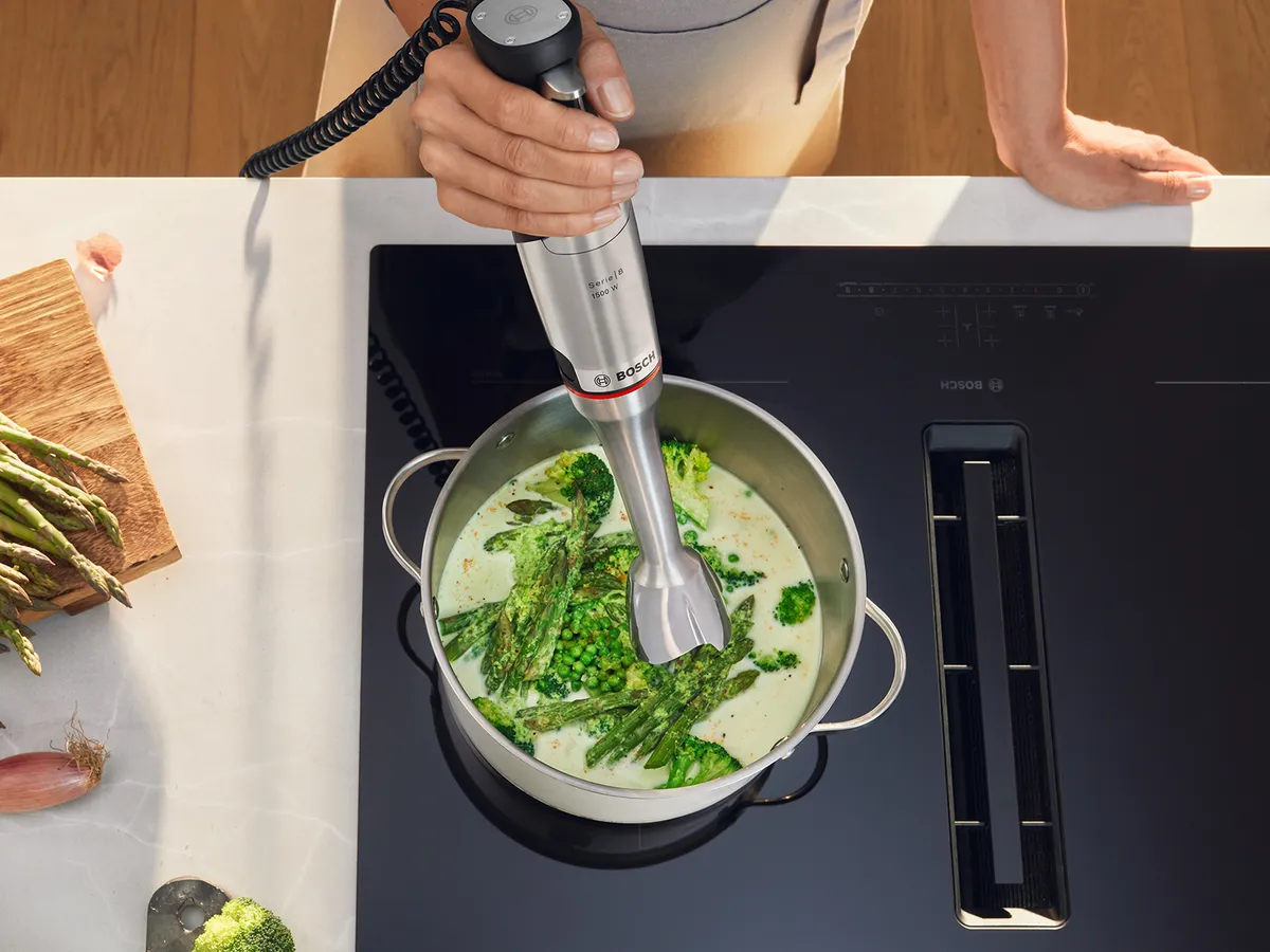 Eine Hand püriert mit dem Bosch Stabmixer grünes Gemüse in einem Topf auf dem Kochfeld.