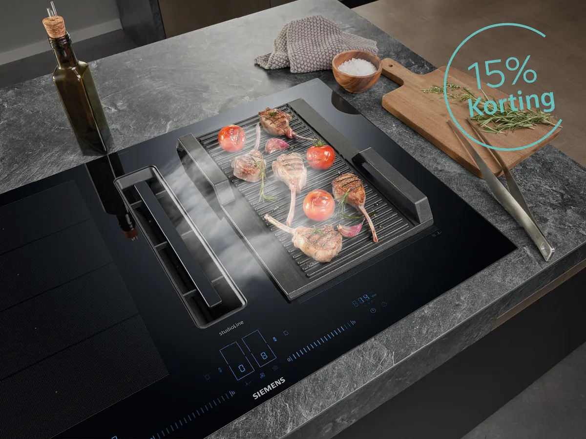 Siemens kookplaat met daarop een grillplaat met lamskoteletjes en tomaat. Aan zijkant olie en houtenplank