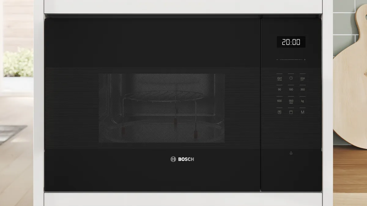 Bosch built-in black microwave with digital control in a modern kitchen cabinet.