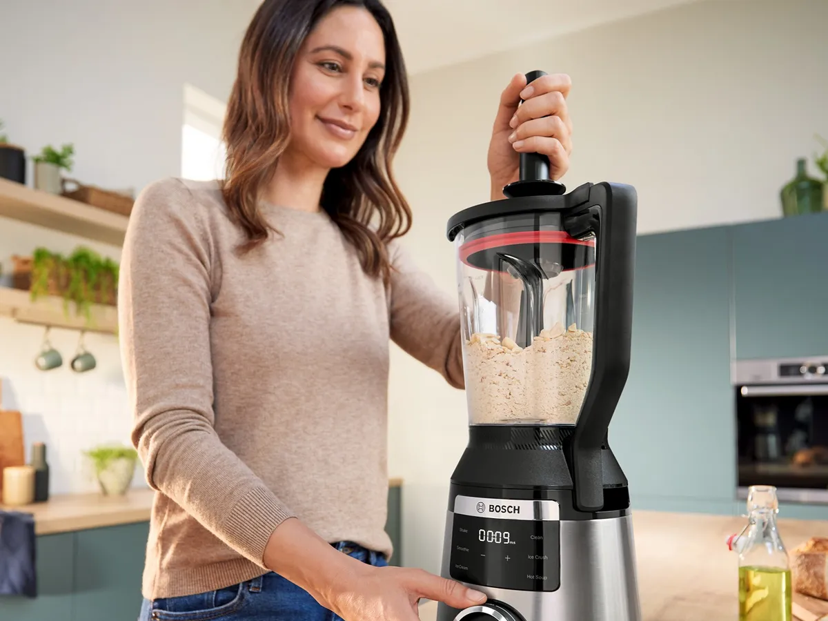 Eine Frau bedient in einer modernen Küche einen mit Haferflocken gefüllten Bosch-Mixer, indem sie einen Knopf drückt.