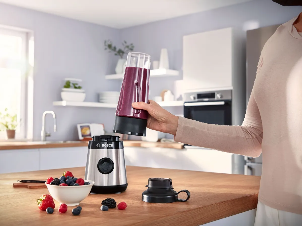 Here's an example:  Hand removing a purple smoothie bottle from a Bosch personal blender, with fresh berries nearby.
