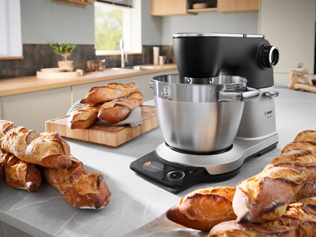 Eine Bosch Küchenmaschine mit integrierter Waage auf einer Arbeitsplatte, umgeben von frisch gebackenen Baguettes.