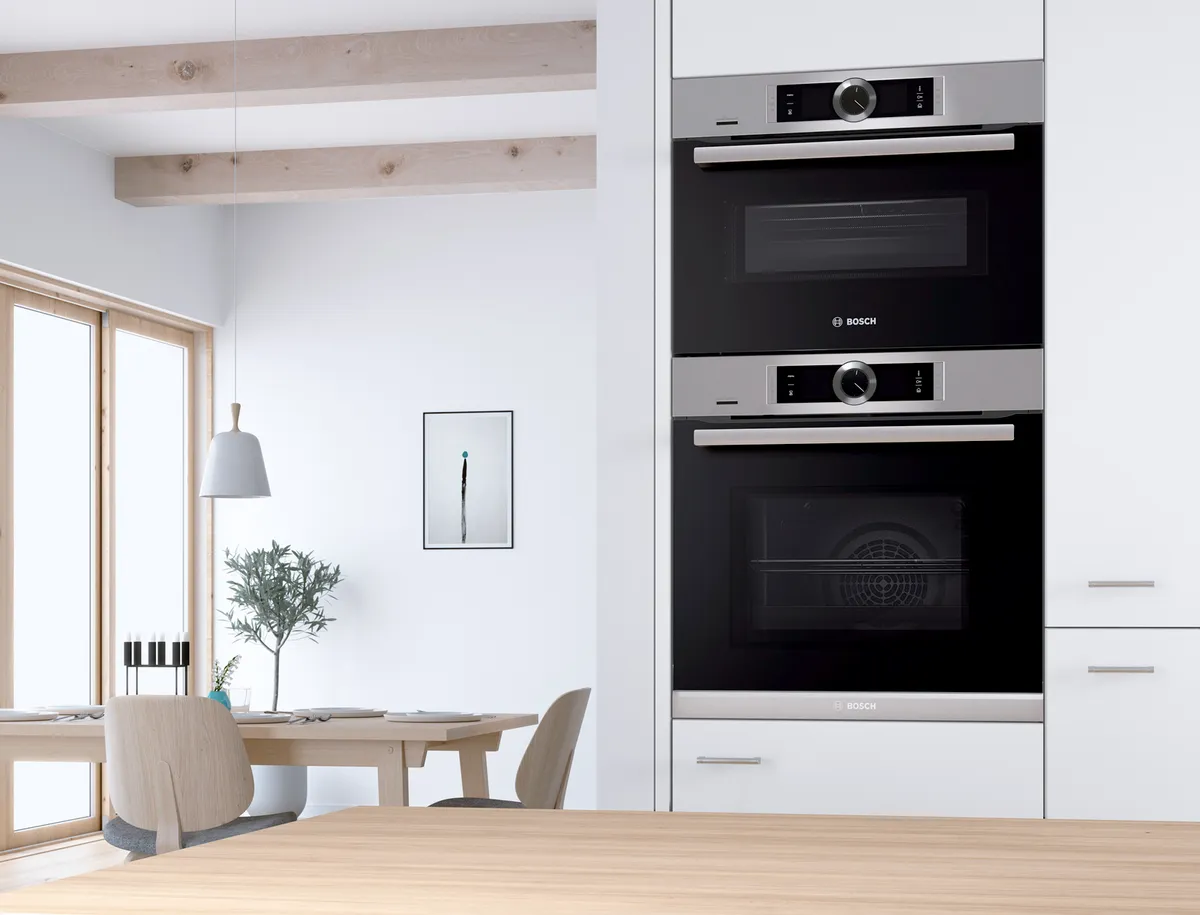 Modern kitchen with Bosch double ovens, wooden beams, dining area, and minimal decor.
