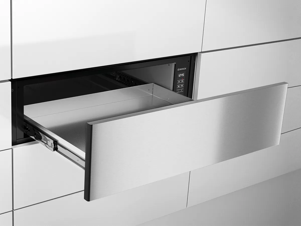 Sleek, built-in Bosch warming drawer in stainless steel, partially opened within a modern, handle-less kitchen cabinetry setup