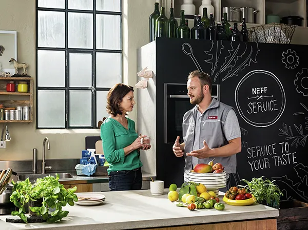 Keuken scene met een man en vrouw bespreken voedselservice, omgeven door verse producten en keukenapparatuur.