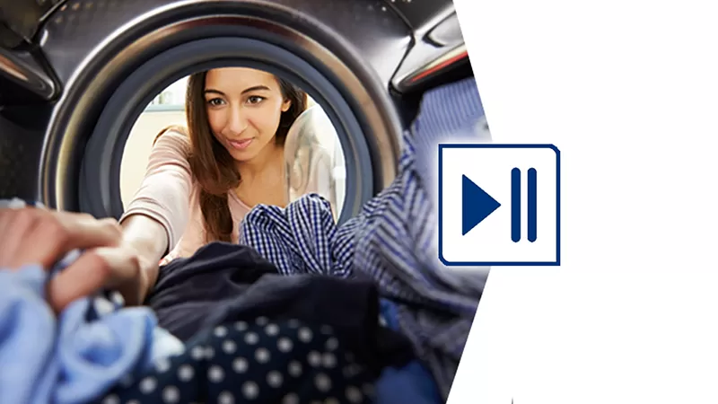 Kadın elbiseleri çamaşır makinesine yüklerken gülümser.