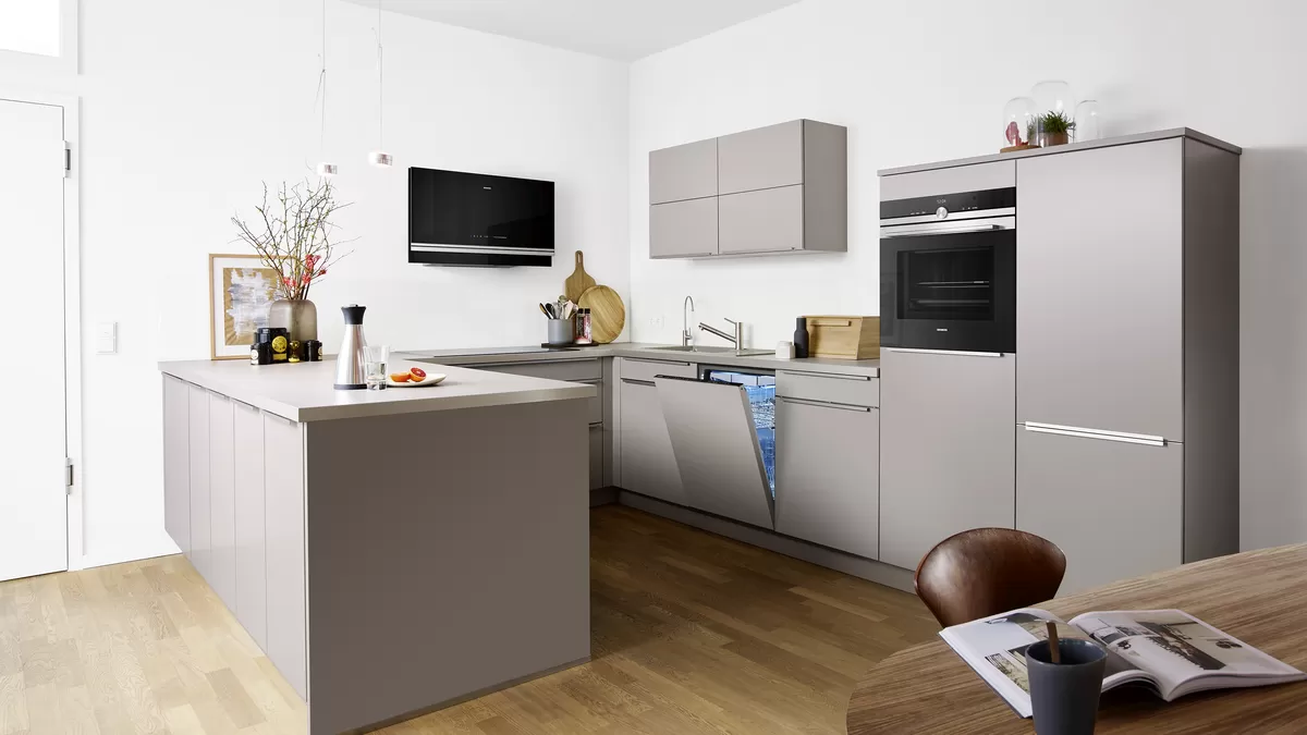 Gri dolaplar, paslanmaz çelik cihazlar ve ahşap zemin ile modern mutfak.