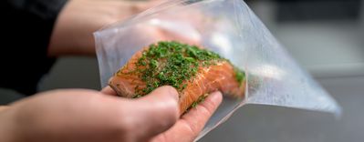Für die Zubereitung im Sous-vide-Backofen wird roher Lachs mit frischen Kräutern von Hand in einen Vakuumierbeutel gegeben.