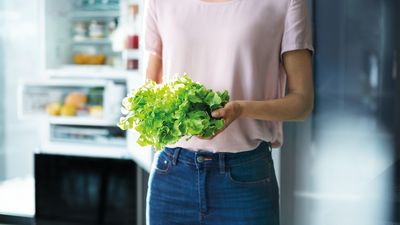Eine Person steht in der Küche und hält einen Salatkopf in der Hand. 