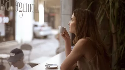 A woman drinking coffee standing next to a window