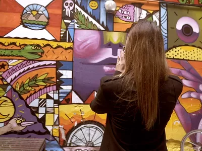 A woman takes a photo of a vibrant mural in an urban alley.