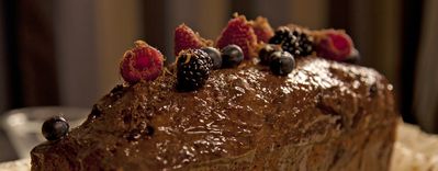 Una ricca torta al cioccolato guarnita con lamponi, more e mirtilli freschi, su uno sfondo scuro ed elegante.