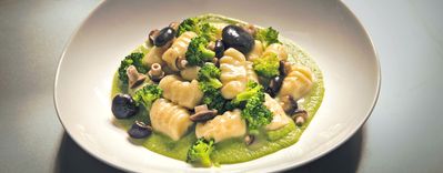 Gnocchi cremosi serviti con broccoli, funghi e olive su una vivace purea verde, presentati in una ciotola bianca.