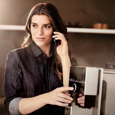 Siemens Coffee World - Donna al telefono accanto a una macchina da espresso completamente automatica silenziosa Siemens EQ.9