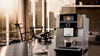 Siemens Kaffeewelt - Ein Siemens EQ.9 Kaffeevollautomat steht auf einem Tisch. Sportausrüstung im Hintergrund.