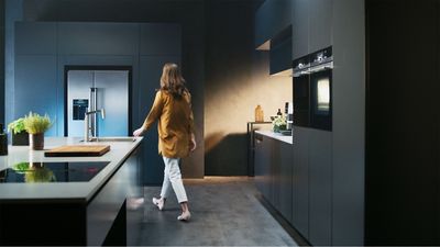 Person walking through dark kitchen with built in appliances and kitchen island in view