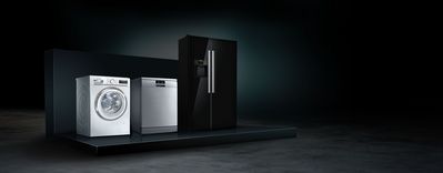 Tri modern&eacute; kuchynsk&eacute; spotrebiče: biela pr&aacute;čka, strieborn&aacute; um&yacute;vačka riadu a elegantn&aacute; čierna chladnička na tmavom pozad&iacute;.