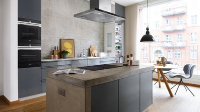 Concrete kitchen island surrounded by numerous built in appliances next to outdoor balcony