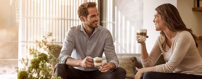 Siemens: due persone sedute su un divano che chiacchierano e bevono un caffè
