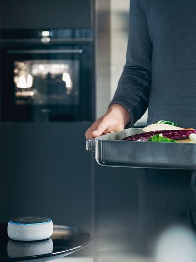 Man holding a baking dish with fish, next to an amazon echo