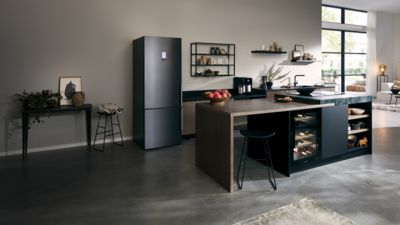 Réfrigérateur noir pose-libre placé dans une cuisine ouverte.
