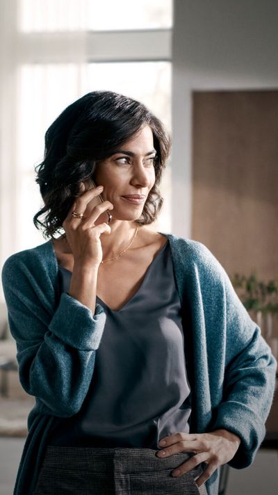 L&auml;chelnde Frau in einem blauen Cardigan, die in einem stylischen Zuhause telefoniert.