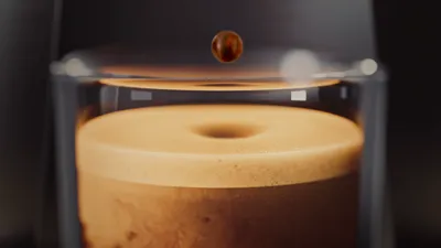 A drop of coffee falls into a glass jar with a freshly brewed espresso and thick crema.