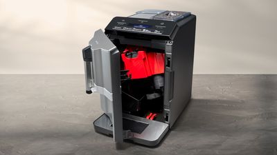 A sleek coffee machine with an open door, revealing a red brewing compartment and control panel on top, set against a neutral background.