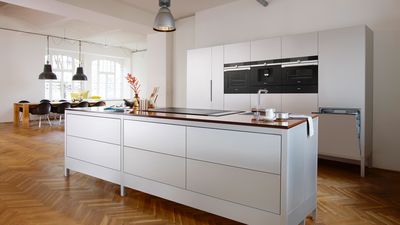 Küchenplanung einer offenen weißen Inselküche, welche sich in einem großen Wohnraum befindet.