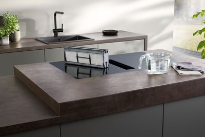 Persona che utilizza il piano cottura a induzione in cucina moderna con piano in legno e lavandino.