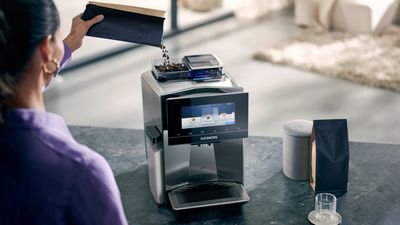 Eine Frau gibt Kaffeebohnen in den Siemens EQ900 Kaffeevollautomaten