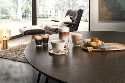 Plusieurs tasses contenant diverses sp&eacute;cialit&eacute;s &agrave; base de caf&eacute;, pos&eacute;es sur une table de salle &agrave; manger et accompagn&eacute;es de g&acirc;teaux.