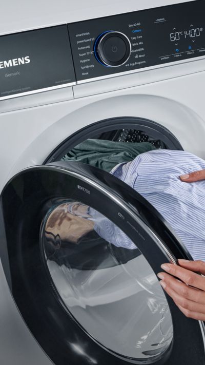 Eine Person legt Wäsche in eine moderne Siemens iQ700 Waschmaschine.