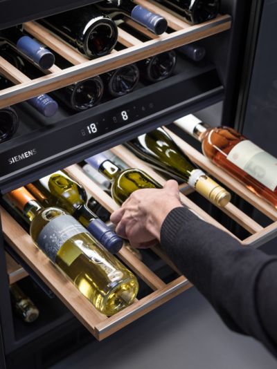 Person interacting with wine bottle in wine cooler