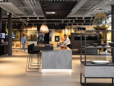 In de Siemens showroom plaatst een vrouw pannen op een kookplaat terwijl een man door de showroom wandelt, omringd door diverse keukenapparaten