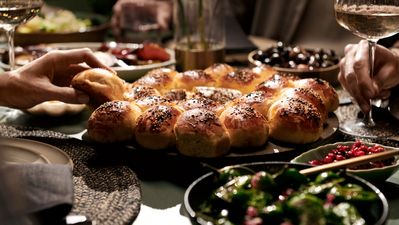 Tafel vol eten waar een vrouw een stukje van de perfect afgebakken breekbrood pakt