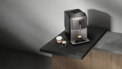 EQ300 stands on a sideboard with black and gray countertop. An espresso stands under the spout, a cappuccino stands next to it.