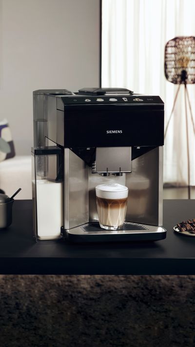 In the foreground the EQ500 with a cappuccino under the outlet is placed on a kitchen island; in the background is a beige couch. 